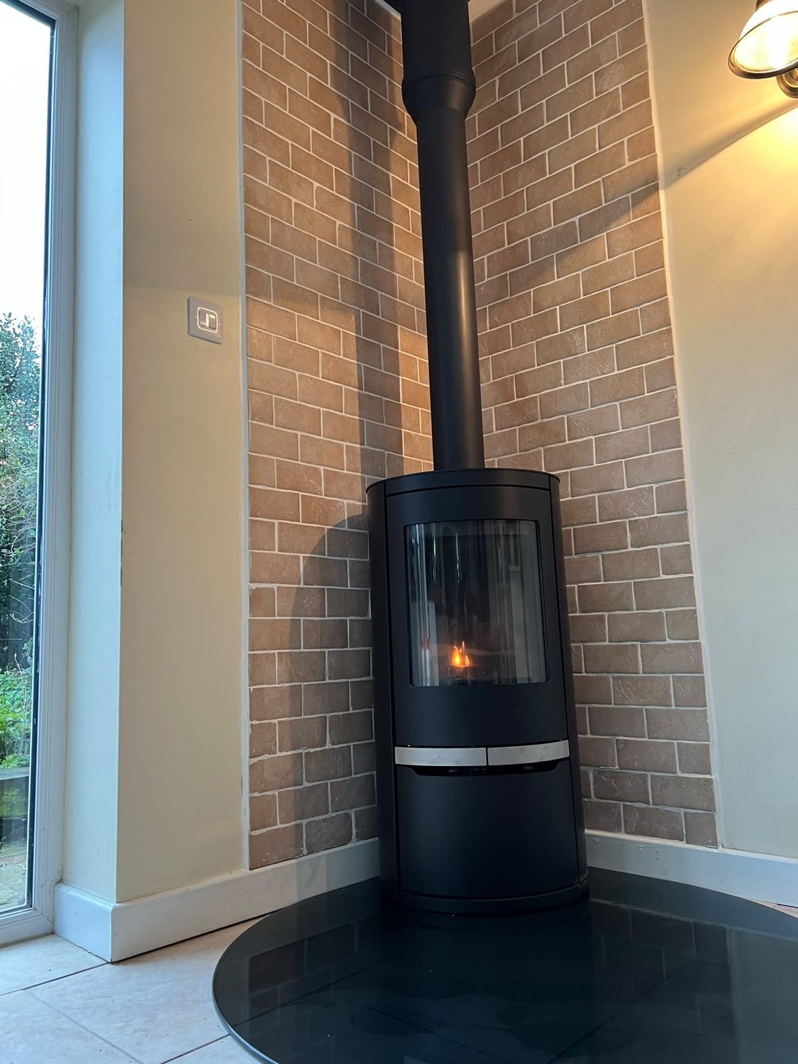 Contemporary curved stove on a black glass hearth against a brick feature wall
