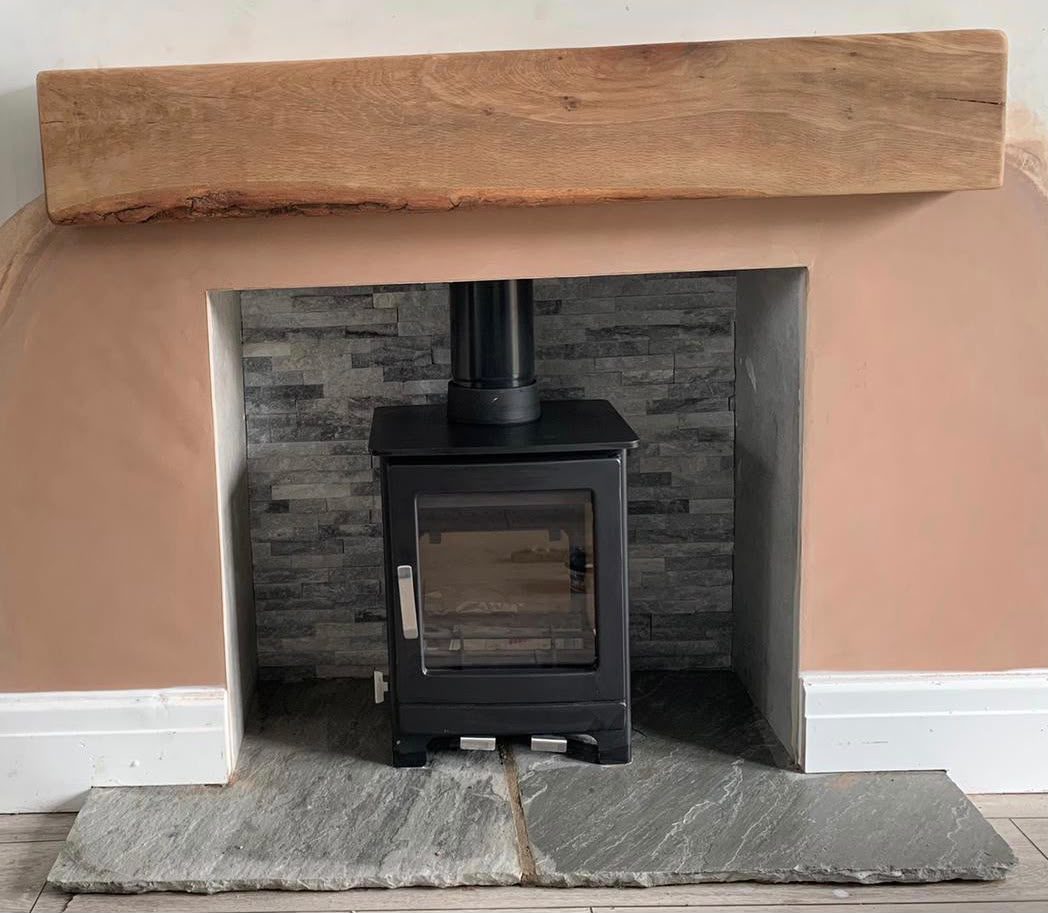 Inset stove in a grey split-face stone breast with a slate hearth and oak beam